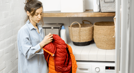 Dame vor der Waschmaschine, welche eine Daunenjacke hält und Fragend die Etikette studiert.
