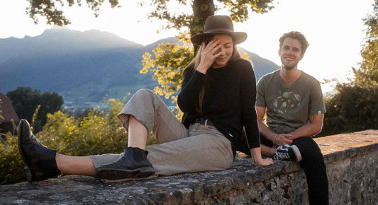 Eine junge Frau und ein junger Mann auf einer Mauer im Hintergrund Bäume und Landschaft