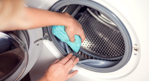 Hände wischen das Innere einer Waschmaschine mit einem Tuch aus
