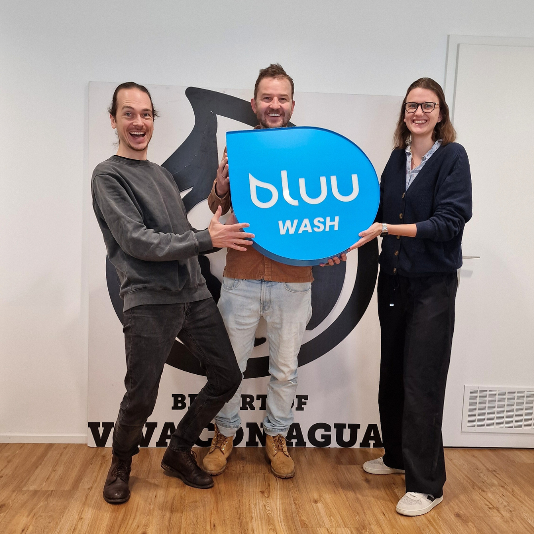 Drei Personen mit bluu-Tropfenlogo vor dem Viva-con-Agua-Banner