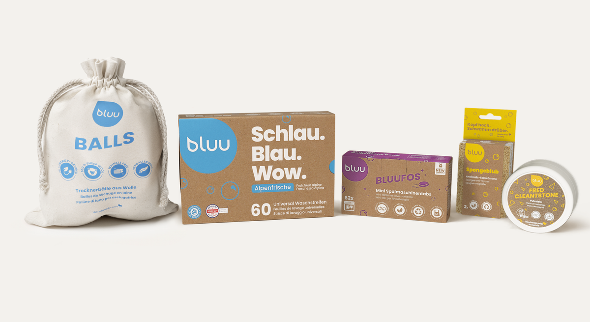 Linea di prodotti su sfondo chiaro: bluu balls nella busta di stoffa, scatola bluu Alpenfrische «Astuto. Blu. Wow.», bluufos, spongeblub e fred cleantstone.