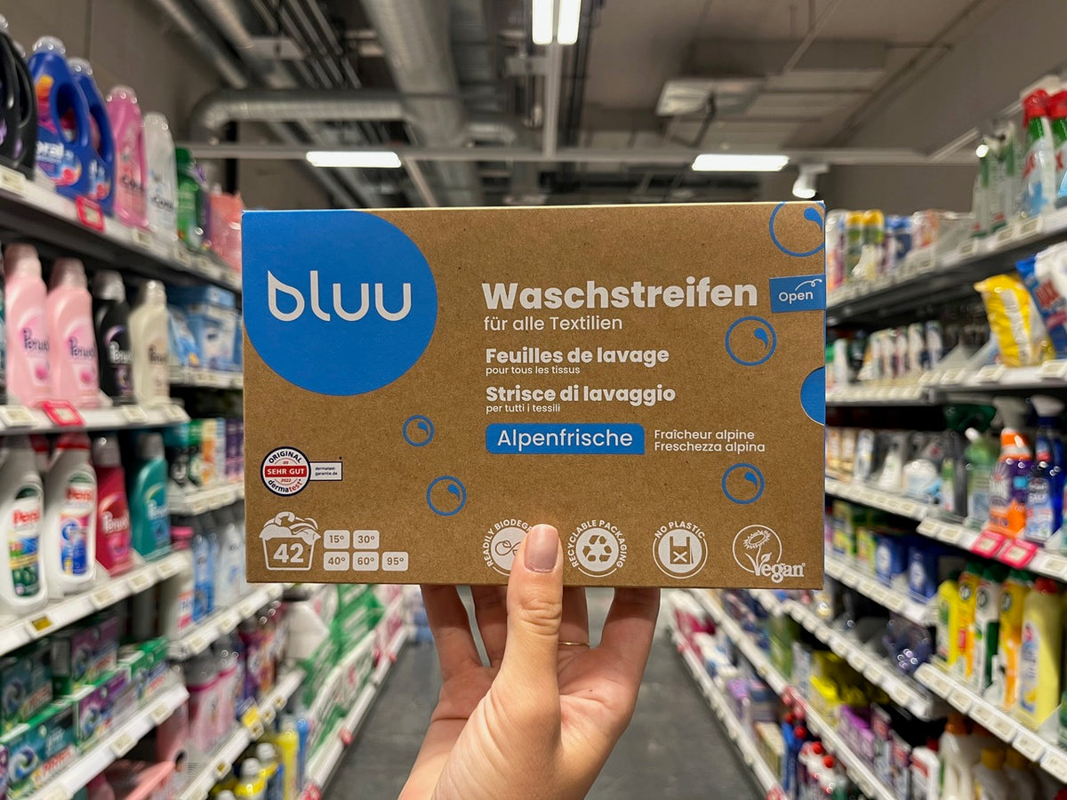 Hand hält eine bluu Waschstreifen-Packung im Supermarktregal